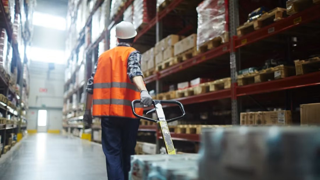 Warehouse operative moving a pallet truck down a racking aisle