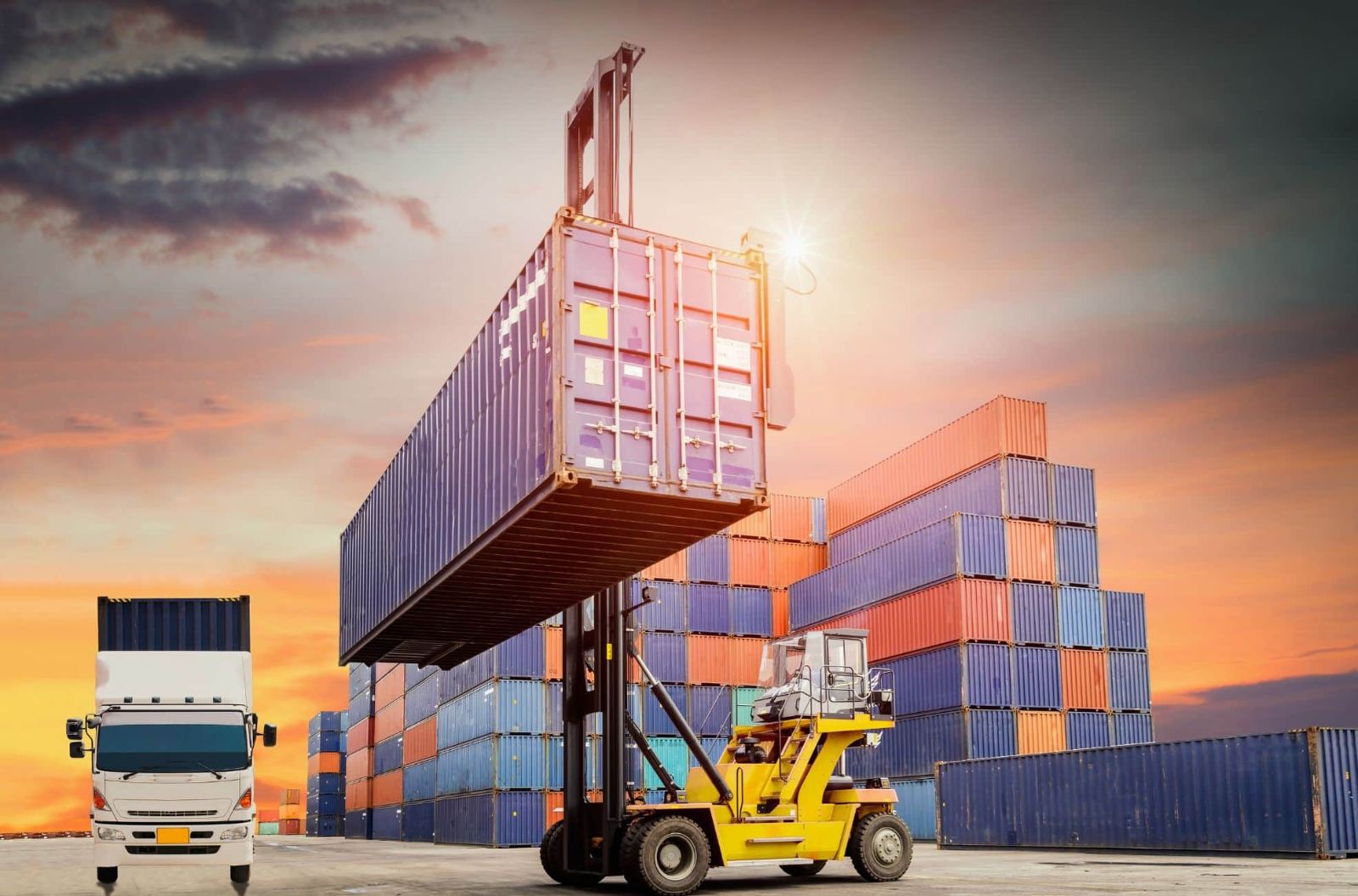 Reach stacker lifting a container in a yard at sunset