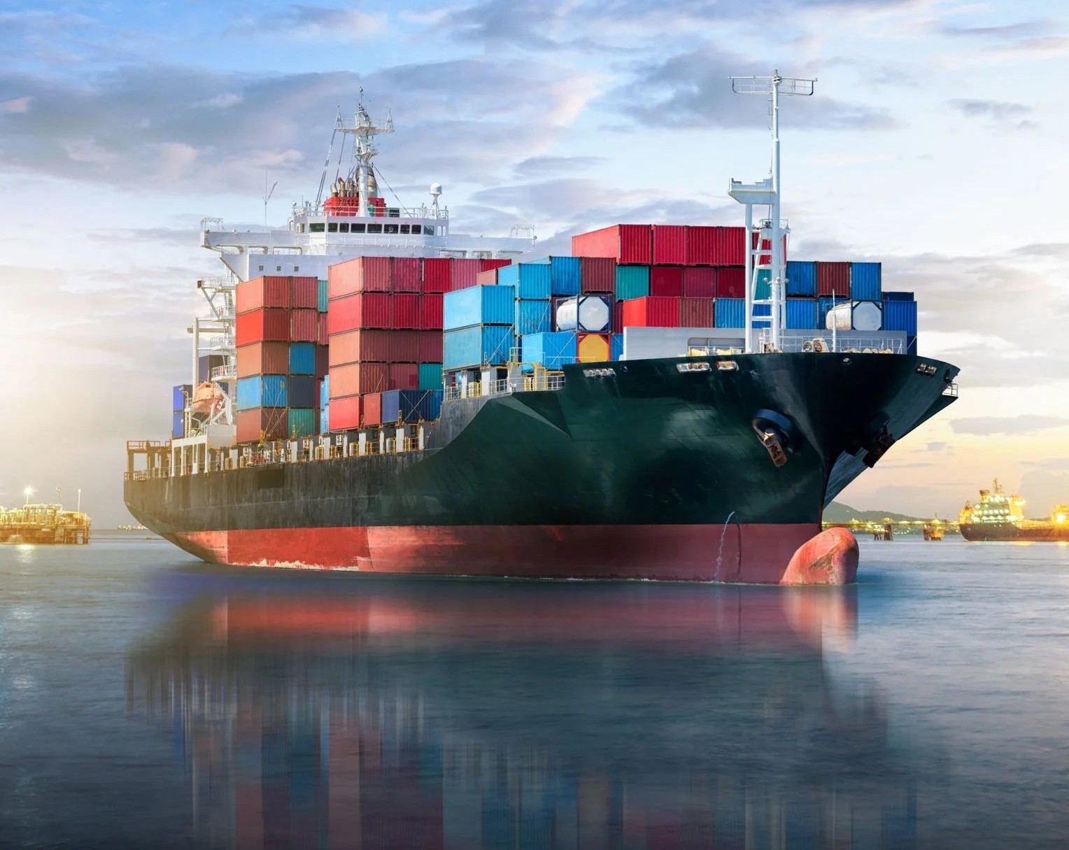 A loaded container vessel approaching a terminal at dusk